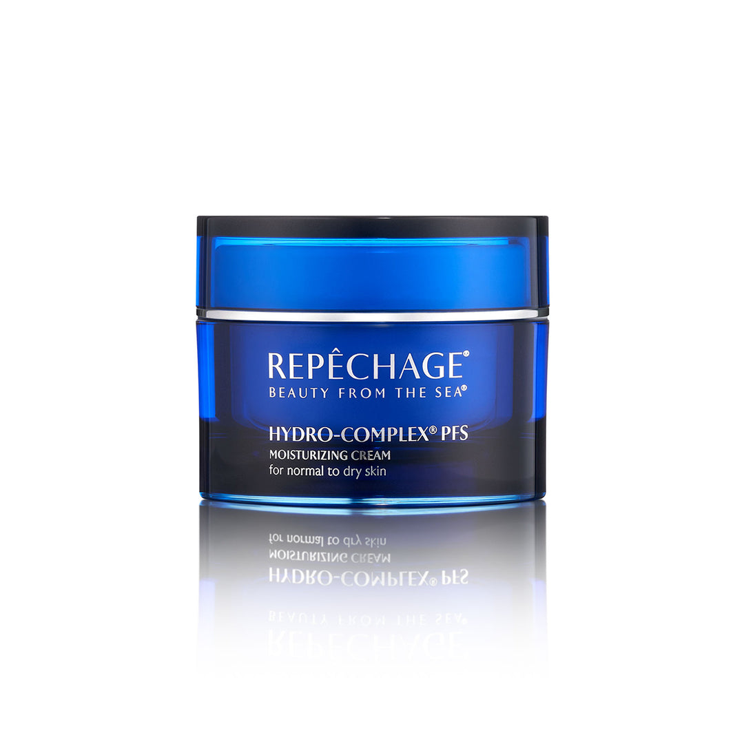 A jar of REPECHAGE Hydro-Complex PFS Moisturizing Cream for dry skin, with blue and white labeling, placed on a reflective surface.