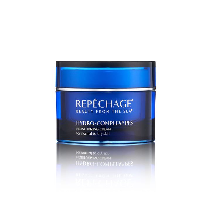 A jar of REPECHAGE Hydro-Complex PFS Moisturizing Cream for dry skin, with blue and white labeling, placed on a reflective surface.