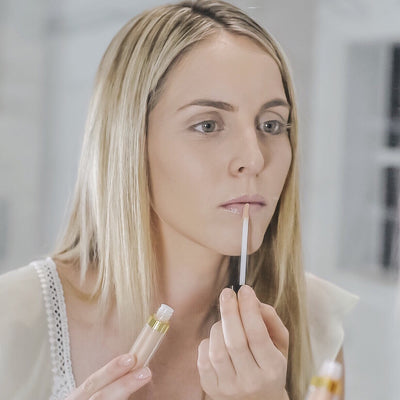 Woman looking in mirror applying Perfect Skin Conditioning Lip Gloss to lip