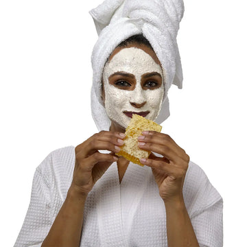 Woman in robe wearing Honey and Almond Scrub holding honeycomb