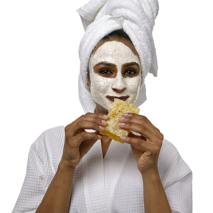 Woman in robe wearing Honey and Almond Scrub holding honeycomb